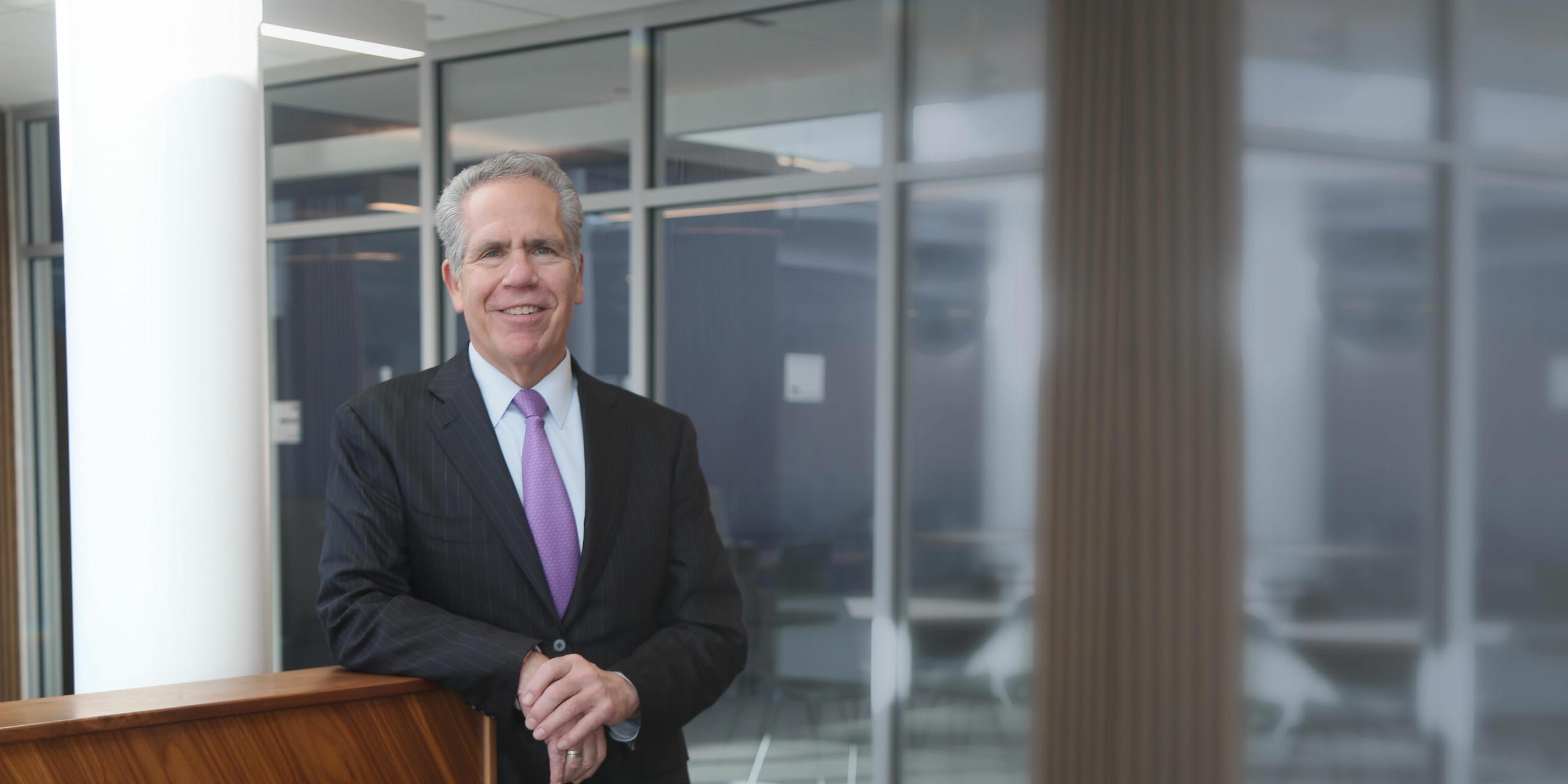 Butler president James danko leaning on a half wall, in gray suit and purple tie